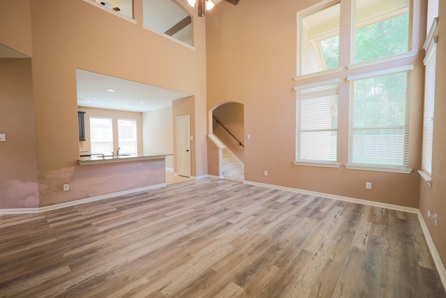 6707 Hunters Creek Ln, Baytown, TX 77521 - unfurnished living room featuring arched walkways, light wood-style flooring, stairway, baseboards, and a towering ceiling