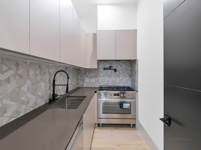 2037 Norfolk St, Houston, TX 77098 - kitchen with stainless steel range with gas cooktop, a sink, dark countertops, light wood-type flooring, and decorative backsplash