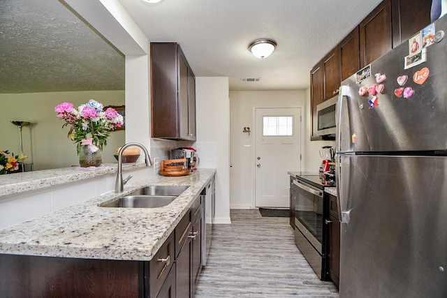 15115 Monrad Dr, Houston, TX 77053 - kitchen featuring appliances with stainless steel finishes, a sink, dark brown cabinets, light wood-style flooring, and a textured ceiling