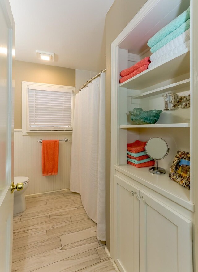 1523 22nd St, Galveston, TX 77550 - full bath featuring wood finished floors, toilet, curtained shower, and a wainscoted wall