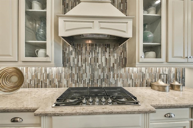 29506 Highland Manor Ct, Katy, TX 77494 - kitchen featuring stainless steel gas stovetop, decorative backsplash, glass insert cabinets, custom range hood, and light stone countertops