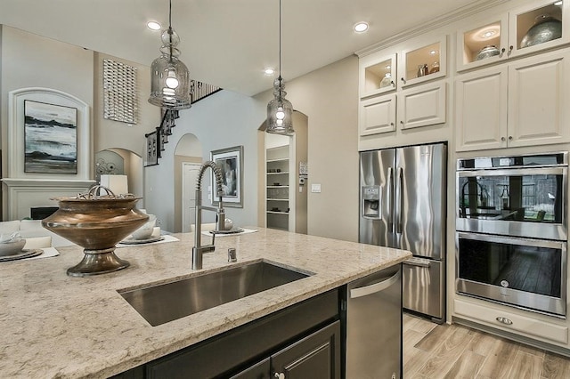 29506 Highland Manor Ct, Katy, TX 77494 - kitchen featuring appliances with stainless steel finishes, a sink, pendant lighting, arched walkways, and light stone counters