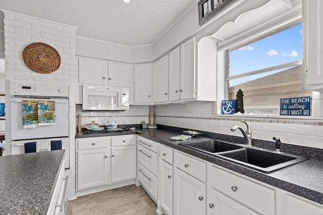 2505 Gerol Dr, Galveston, TX 77551 - kitchen featuring white appliances, a sink, dark countertops, white cabinetry, and a textured ceiling