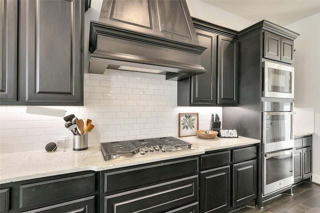 18115 Bachman Branch Dr, Cypress, TX 77433 - kitchen with appliances with stainless steel finishes, custom range hood, backsplash, light stone counters, and dark wood-type flooring