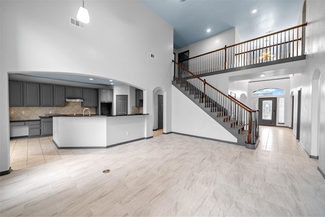 13909 Stonewood Ct, Rosharon, TX 77583 - unfurnished living room featuring a high ceiling, arched walkways, stairs, a sink, and baseboards
