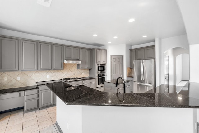13909 Stonewood Ct, Rosharon, TX 77583 - kitchen with appliances with stainless steel finishes, a large island with sink, arched walkways, under cabinet range hood, and backsplash