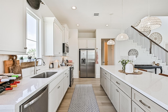 4101 5th St, Galveston, TX 77554 - kitchen featuring appliances with stainless steel finishes, a sink, hanging light fixtures, white cabinetry, and light wood-style floors