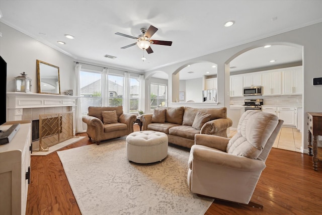9110 Kinnel Ln, Tomball, TX 77375 - living area with ceiling fan, wood finished floors, crown molding, a tiled fireplace, and arched walkways