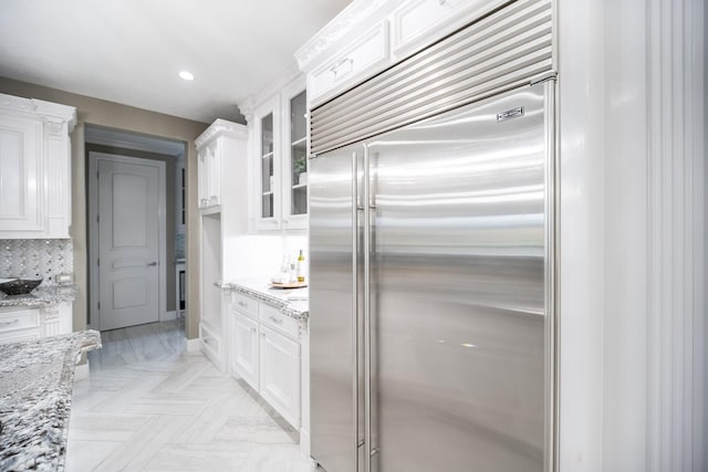 10887 Decatur St, Willis, TX 77318 - kitchen with built in refrigerator, white cabinets, glass insert cabinets, light stone countertops, and recessed lighting