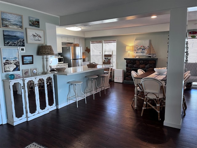 16627 Bermuda Way, Jamaica Beach, TX 77554 - kitchen with freestanding refrigerator, a peninsula, dark wood-style floors, a kitchen breakfast bar, and white cabinetry