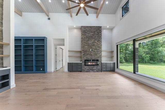 15086 Dewberry Ln, Conroe, TX 77302 - unfurnished living room featuring a fireplace, a ceiling fan, a towering ceiling, light wood-type flooring, and wooden ceiling with exposed beams