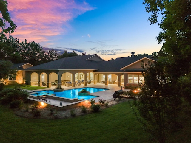12911 Mossy Shr, Tomball, TX 77375 - back of house at dusk featuring a patio area, a lawn, an outdoor pool, and a chimney