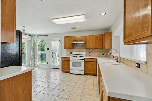 19710 Ringwald Ct, Spring, TX 77379 - kitchen with white gas stove, a sink, tasteful backsplash, brown cabinets, and under cabinet range hood