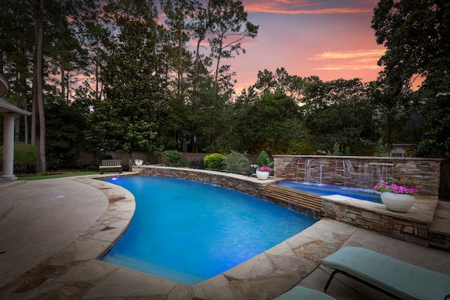 63 N Wooded Brook Cir, The Woodlands, TX 77382 - pool at dusk with an in-ground hot tub, a patio area, a fenced backyard, and view of wooded area