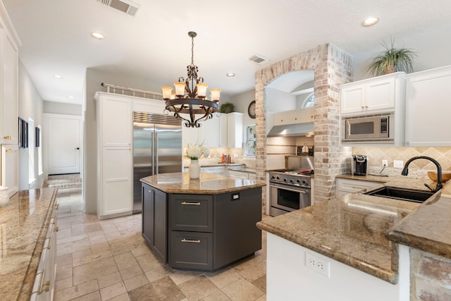 63 N Wooded Brook Cir, The Woodlands, TX 77382 - kitchen with built in appliances, a sink, under cabinet range hood, white cabinetry, and backsplash