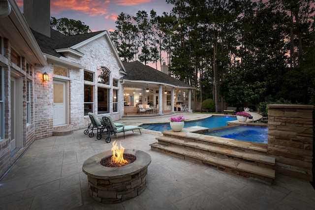 63 N Wooded Brook Cir, The Woodlands, TX 77382 - pool at dusk featuring a fire pit, an outdoor pool, a patio area, and ceiling fan