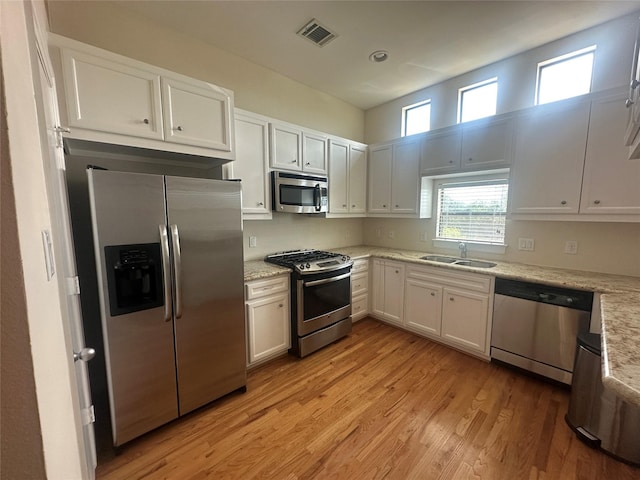8710 Beverlyhill St Unit 102, Houston, TX 77063 - kitchen with stainless steel appliances, a sink, light wood finished floors, white cabinetry, and light stone counters