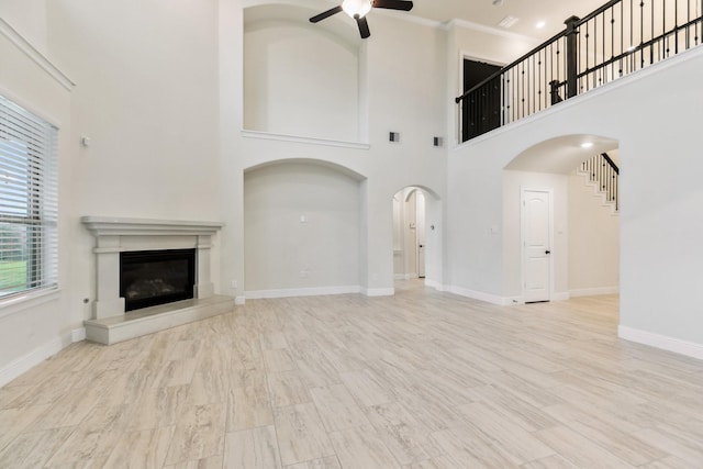 15411 Patten Forest Dr, Cypress, TX 77429 - unfurnished living room featuring ceiling fan, arched walkways, a glass covered fireplace, a towering ceiling, and baseboards