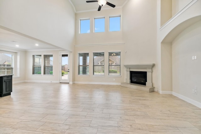 15411 Patten Forest Dr, Cypress, TX 77429 - unfurnished living room featuring ceiling fan, a glass covered fireplace, ornamental molding, plenty of natural light, and a towering ceiling