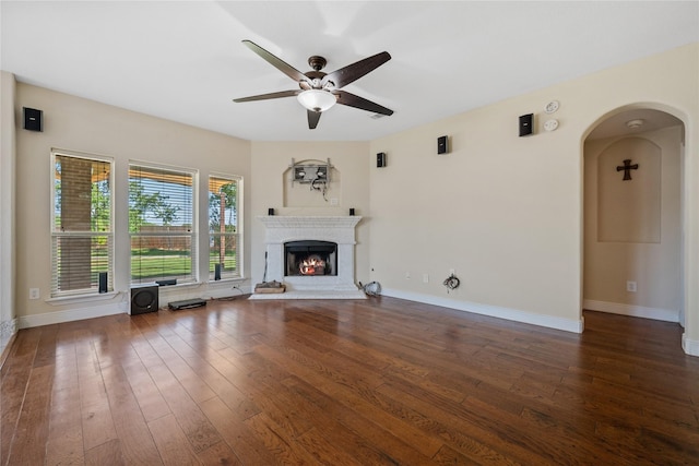 8002 Elm Wood Ct, Baytown, TX 77523 - unfurnished living room featuring a ceiling fan, arched walkways, wood-type flooring, baseboards, and a warm lit fireplace