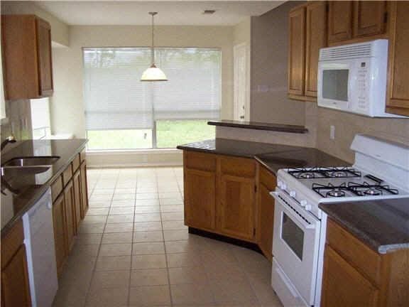 7631 Ashton Dr, Houston, TX 77095 - kitchen with white appliances, a sink, brown cabinets, and dark countertops