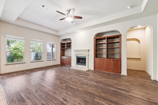 107 N Greenprint Cir, Tomball, TX 77375 - unfurnished living room with a raised ceiling, built in shelves, a ceiling fan, wood finished floors, and a fireplace with raised hearth