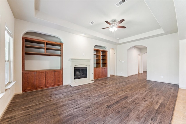 107 N Greenprint Cir, Tomball, TX 77375 - unfurnished living room with a tray ceiling, a ceiling fan, wood finished floors, a fireplace with raised hearth, and built in features