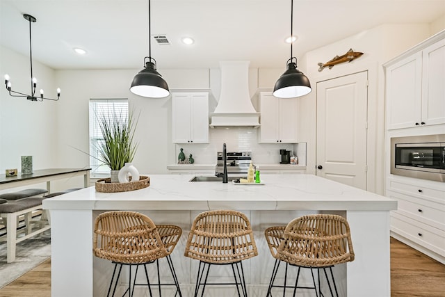 2515 103rd St, Galveston, TX 77554 - kitchen featuring a sink, stainless steel microwave, custom range hood, an island with sink, and white cabinets