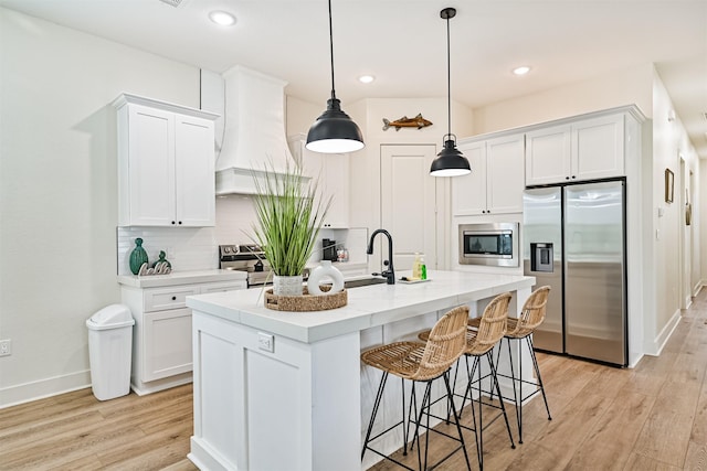 2515 103rd St, Galveston, TX 77554 - kitchen featuring appliances with stainless steel finishes, premium range hood, light wood-style floors, white cabinets, and a breakfast bar area
