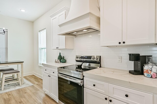 2515 103rd St, Galveston, TX 77554 - kitchen with stainless steel electric stove, premium range hood, light wood-style floors, white cabinetry, and light stone counters