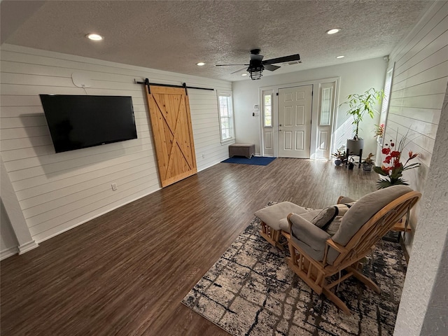 2044 Des Jardines St, Houston, TX 77023 - living room featuring a barn door, wooden walls, wood finished floors, a textured ceiling, and a ceiling fan
