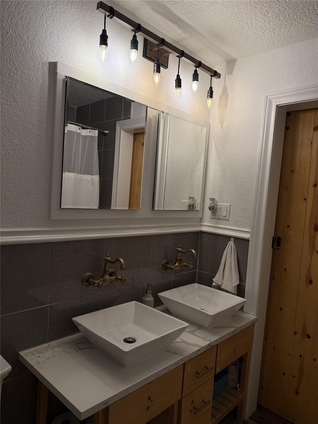 2044 Des Jardines St, Houston, TX 77023 - bathroom with a textured ceiling, double vanity, tile walls, a textured wall, and wainscoting