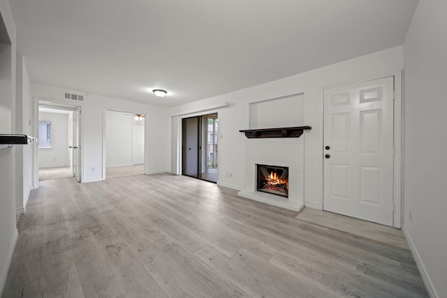 3500 Tangle Brush Dr Unit 48, The Woodlands, TX 77381 - unfurnished living room with a brick fireplace, light wood-style flooring, and baseboards
