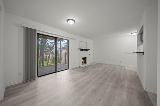 3500 Tangle Brush Dr Unit 48, The Woodlands, TX 77381 - unfurnished living room with light wood finished floors, a lit fireplace, and baseboards