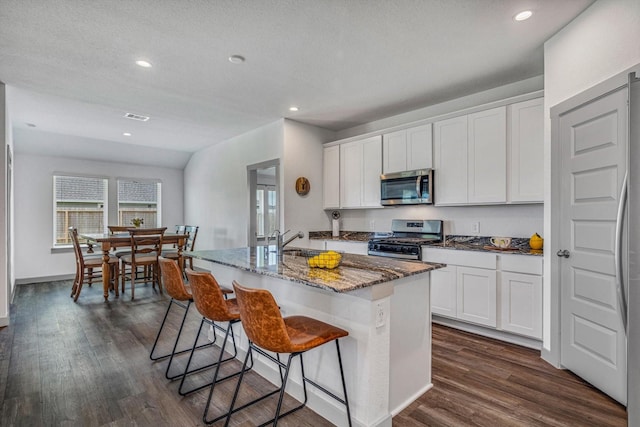1709 Perch St, Alvin, TX 77511 - kitchen featuring appliances with stainless steel finishes, a sink, dark wood-type flooring, stone countertops, and an island with sink