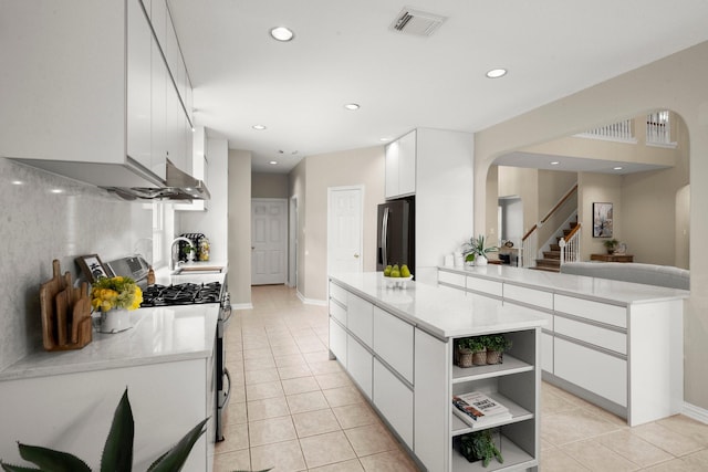9607 Woodcliff Lake Dr, Spring, TX 77379 - kitchen featuring arched walkways, stainless steel gas range oven, refrigerator with ice dispenser, light tile patterned floors, and recessed lighting