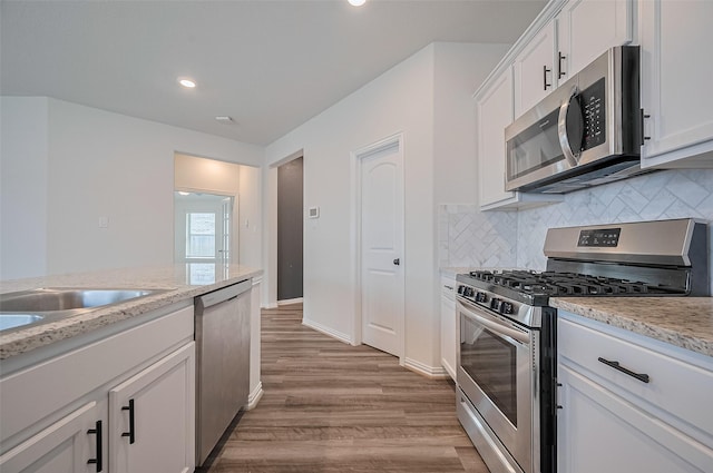 20231 Creekdale Bend Dr, Cypress, TX 77433 - kitchen featuring appliances with stainless steel finishes, wood finished floors, tasteful backsplash, white cabinetry, and light stone counters