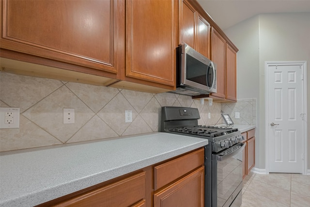 13409 Timberoak Ct, Rosharon, TX 77583 - kitchen featuring black range with gas stovetop, stainless steel microwave, light countertops, light tile patterned flooring, and brown cabinets