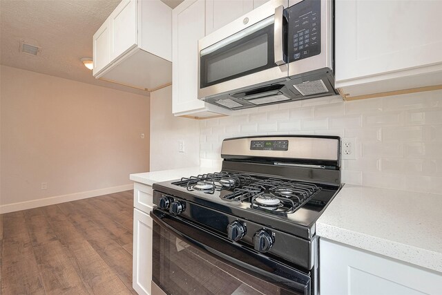 12111 Jutland Rd, Houston, TX 77048 - kitchen featuring black gas range, stainless steel microwave, backsplash, and dark wood-style floors