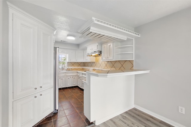 1118 Hammock St, Houston, TX 77009 - kitchen with under cabinet range hood, backsplash, a peninsula, white cabinetry, and light countertops