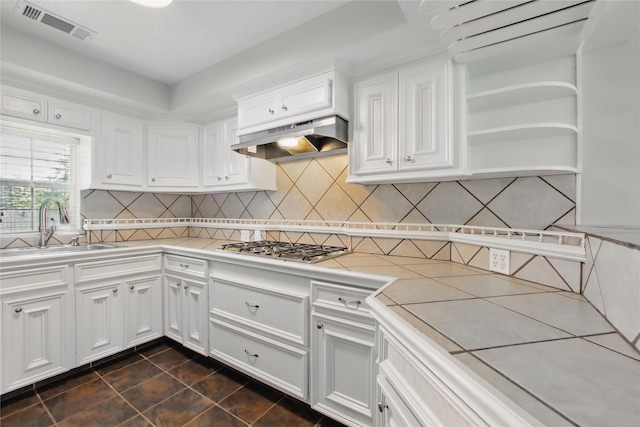 1118 Hammock St, Houston, TX 77009 - kitchen featuring under cabinet range hood, white cabinets, stainless steel gas cooktop, dark tile patterned floors, and a sink