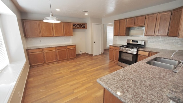 1203 Brook Grove Dr, Katy, TX 77450 - kitchen with stainless steel gas range oven, brown cabinets, a sink, decorative backsplash, and light wood finished floors