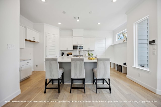 1816 Colquitt St, Houston, TX 77098 - kitchen with stainless steel microwave, white cabinetry, light countertops, an island with sink, and a breakfast bar