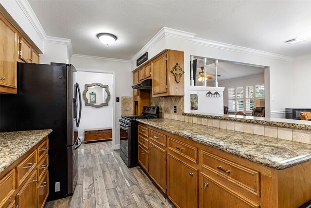 3303 Indian Mound Trl, Crosby, TX 77532 - kitchen with black gas range oven, freestanding refrigerator, under cabinet range hood, tasteful backsplash, and light wood finished floors