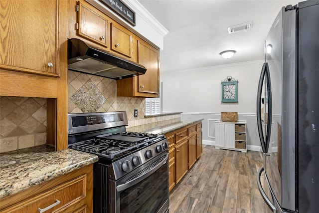 3303 Indian Mound Trl, Crosby, TX 77532 - kitchen with stainless steel appliances, under cabinet range hood, crown molding, brown cabinetry, and dark wood-style flooring