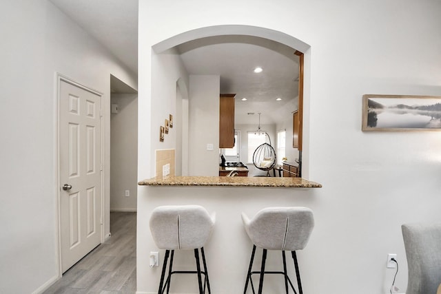 12943 Palm Leaf Ct, Houston, TX 77044 - kitchen featuring arched walkways, a kitchen breakfast bar, light wood-style floors, recessed lighting, and brown cabinets
