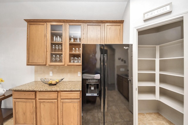 12943 Palm Leaf Ct, Houston, TX 77044 - kitchen with black fridge, backsplash, light stone countertops, glass insert cabinets, and light tile patterned floors