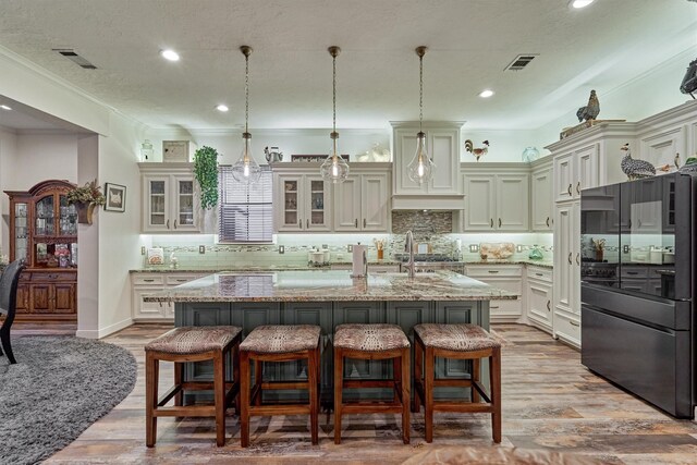 167 Monterrey Rd E, Montgomery, TX 77356 - kitchen featuring freestanding refrigerator, an island with sink, light stone counters, a kitchen bar, and recessed lighting