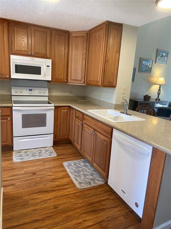 8435 Sands Point Dr, Houston, TX 77036 - kitchen featuring white appliances, a sink, dark wood-style floors, a textured ceiling, and a peninsula