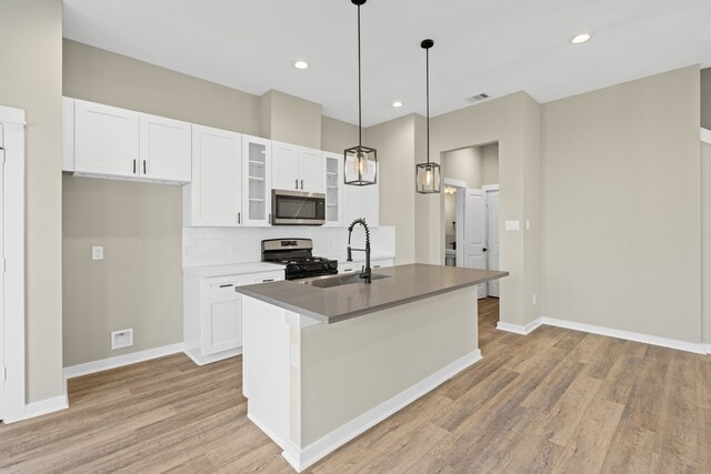 11326 Stonework Grove Ln, Houston, TX 77076 - kitchen featuring stainless steel microwave, a sink, range with gas stovetop, light wood-style floors, and a kitchen island with sink